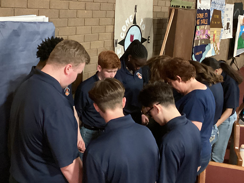 Students in blue shirts huddled together in prayer.